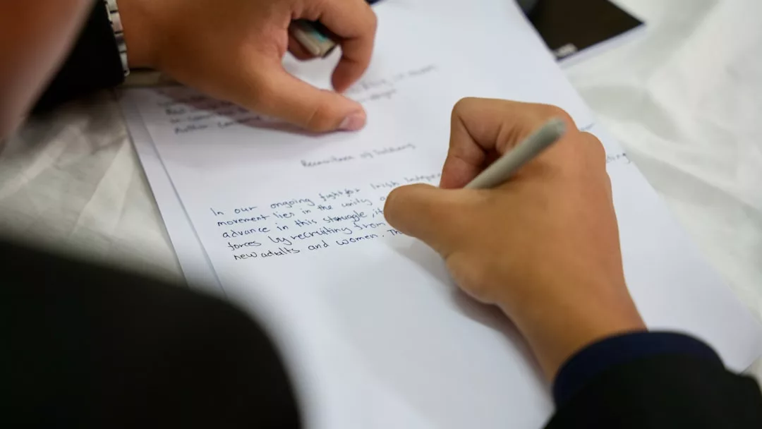 Una persona escribe con un bolígrafo sobre una hoja manuscrita, encarnando el tranquilo lujo de Mallorca, mientras otra mano descansa suavemente sobre el papel.