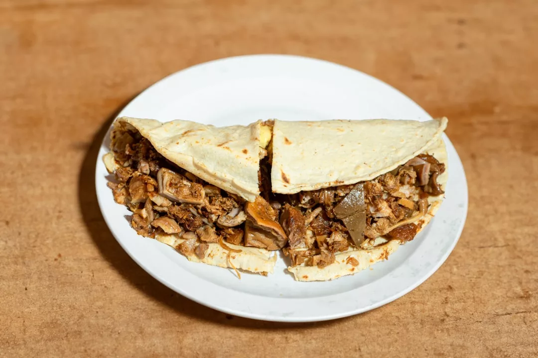 Una tortilla de maíz doblada por la mitad y rellena de carne picada y vísceras, servida en un plato blanco sobre una superficie de madera: una sencilla pero sabrosa muestra de la comida callejera de Mallorca, que aporta un inesperado toque de lujo a cada bocado.