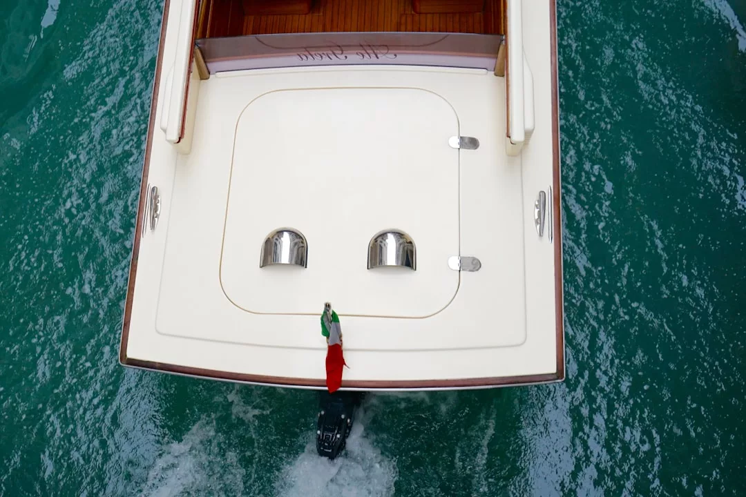 Vista aérea de la popa de un yate con una bandera italiana, dos respiraderos y un motor en aguas turquesas, capturando el espíritu del lujo mientras navega cerca de Mallorca.