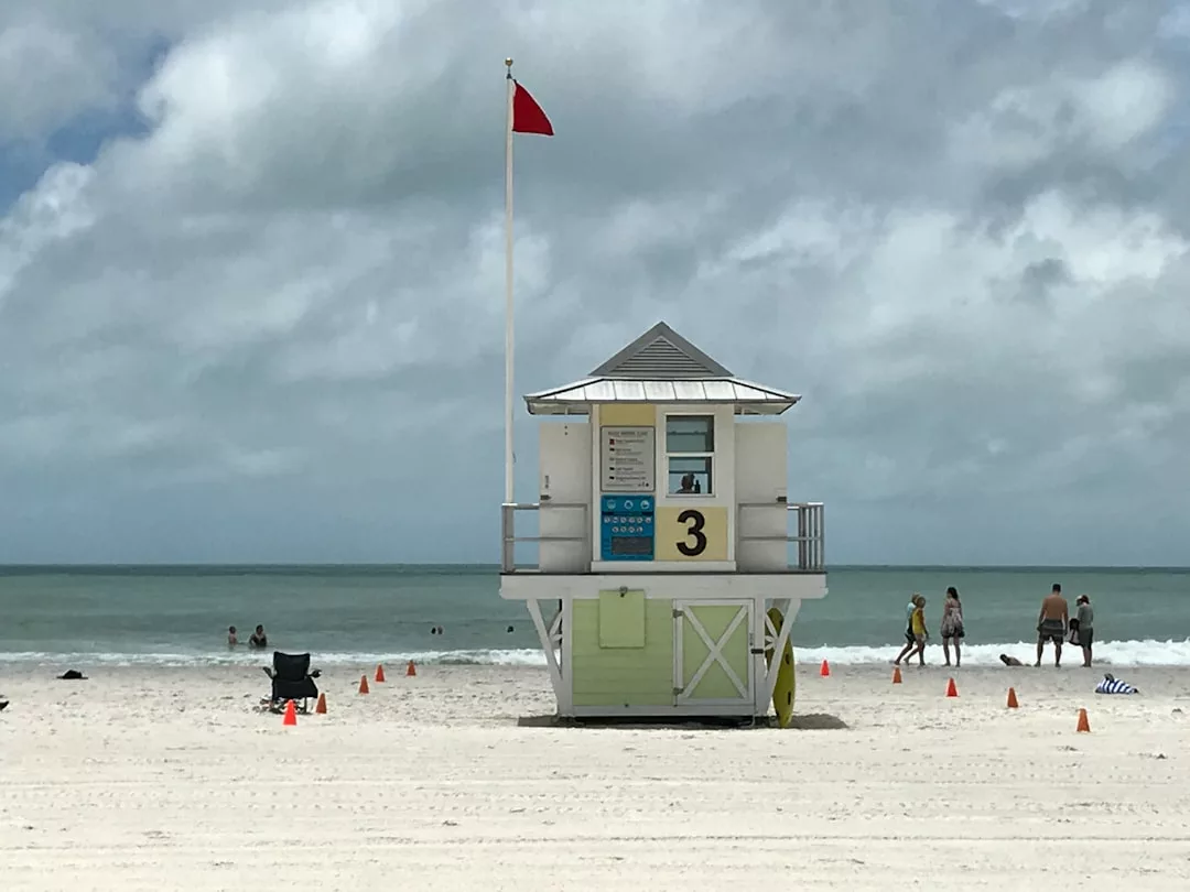 Torre de salvamento número 3 con bandera roja en la playa de arena de Mallorca, gente disfrutando del lujo del sol y el surf, bajo un cielo nublado.