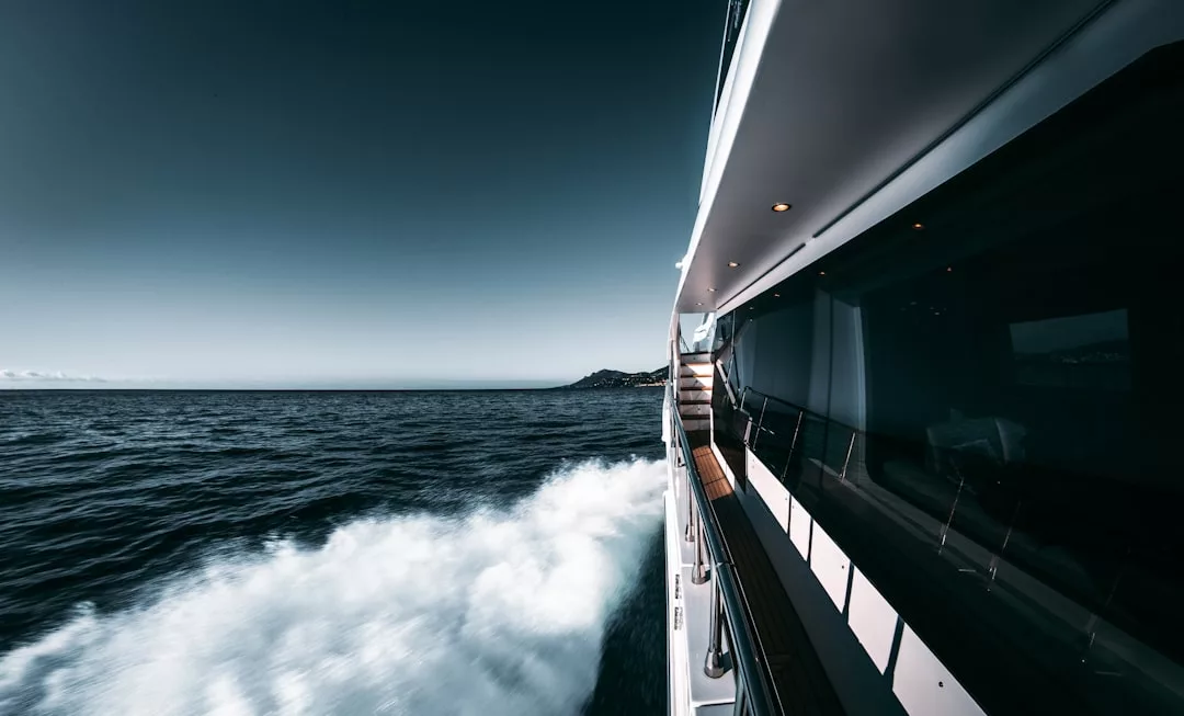 Vista desde el lateral de un yate de lujo que surca a toda velocidad el océano cerca de Mallorca, con agua pulverizada en el aire y una costa lejana bajo un cielo despejado.
