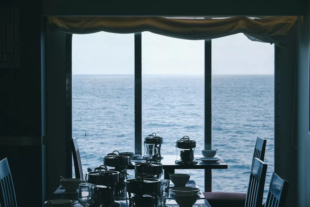 Mesa de comedor con platos y ollas cerca de grandes ventanales con vistas al océano en un luminoso día de Mallorca, añadiendo un toque de lujo a su experiencia gastronómica.