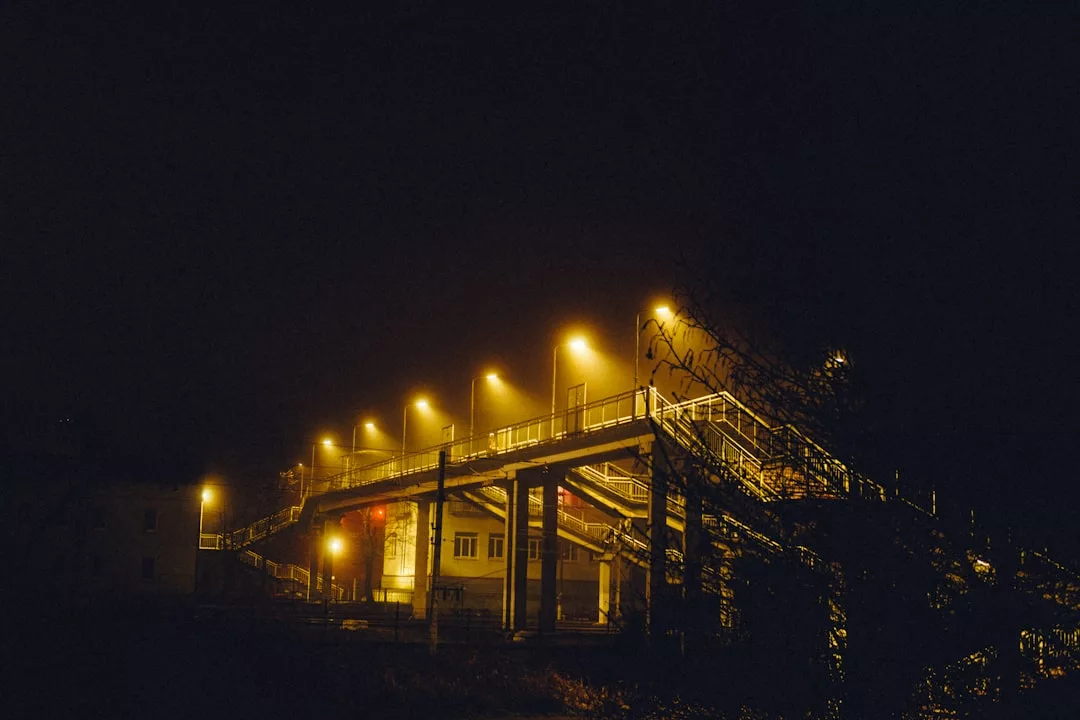 Un paso de peatones elevado es iluminado por múltiples farolas amarillas por la noche en Mallorca, con un edificio visible bajo la estructura, evocando una sensación de lujo y sofisticación.