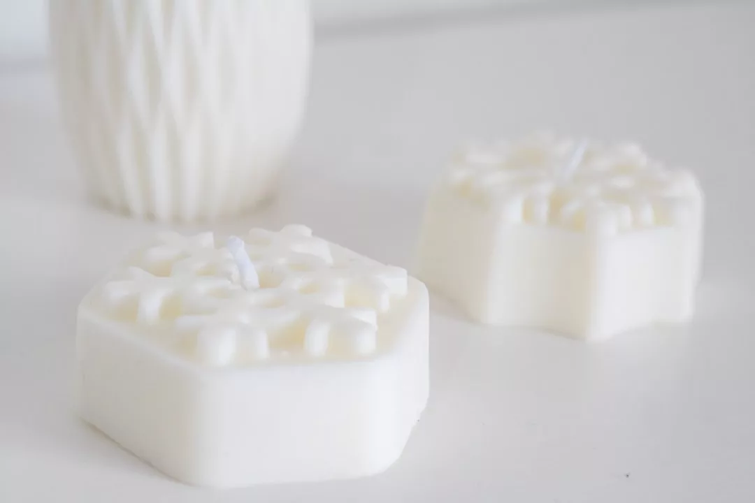 Dos jabones hexagonales blancos con un diseño de copo de nieve en relieve se asientan sobre una superficie blanca; evocando el refinado Lujo de Mallorca, un recipiente blanco texturizado se difumina en el fondo.