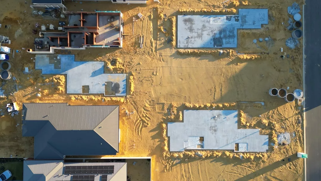 Vista aérea de una obra en construcción en Mallorca que muestra varios cimientos de edificios y una estructura de lujo terminada y techada, rodeada de arena y materiales de construcción.