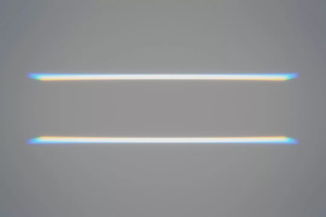 Dos líneas blancas horizontales paralelas con un tenue resplandor de arco iris en sus bordes evocan una sensación de lujo, colocadas con elegancia sobre un fondo gris liso que recuerda la serena sencillez de Mallorca.