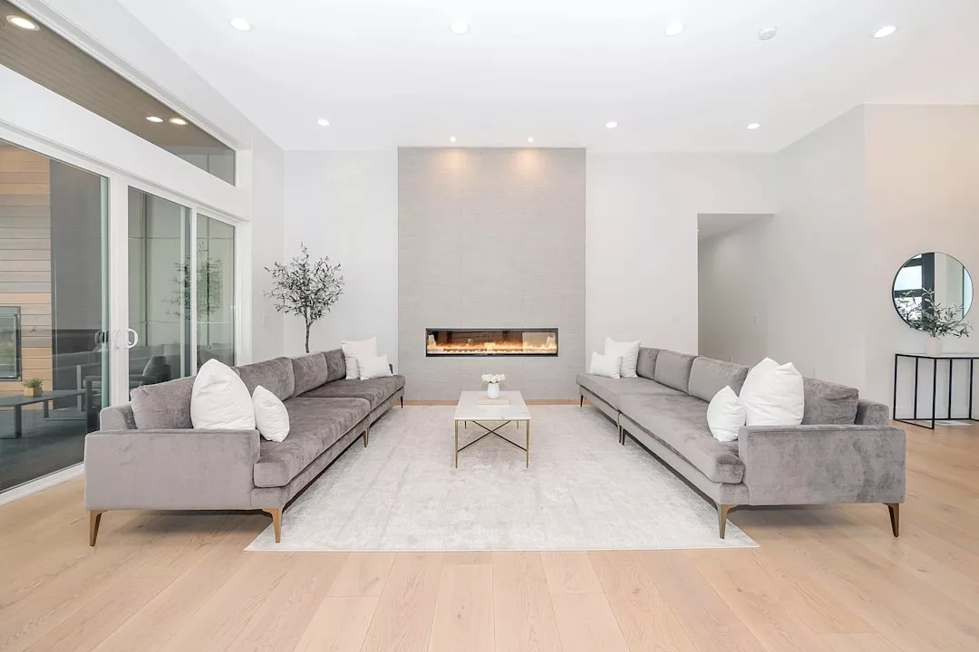 Moderno salón con dos sofás grises enfrentados, una chimenea de pared, una alfombra blanca y una pequeña mesa de centro. Este espacio inspirado en Mallorca desprende lujo por su paleta de colores neutros y su decoración minimalista.