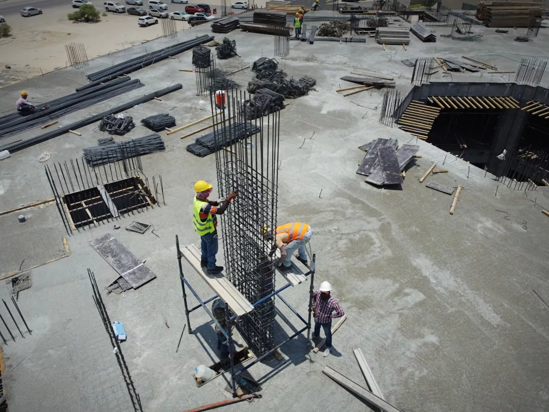 Cuatro obreros de la construcción con equipo de seguridad montan una columna de hormigón armado en un andamio, rodeados de materiales y barras de refuerzo en una obra de Mallorca, lo que refleja la precisión necesaria para los proyectos de construcción de lujo.