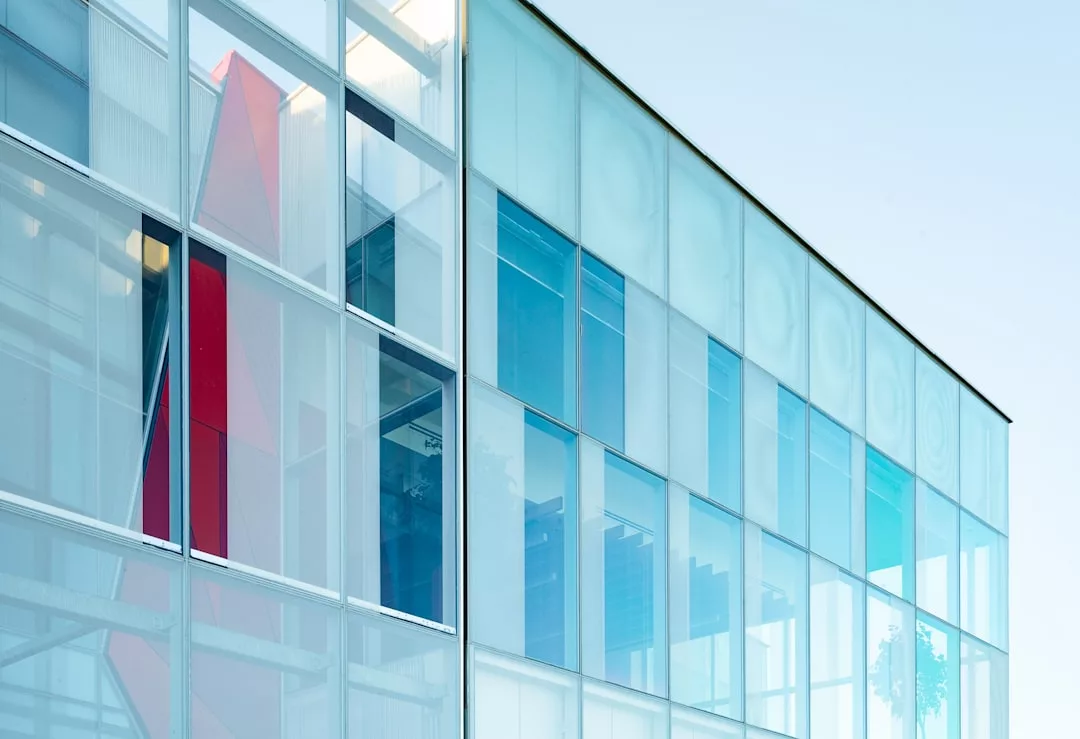 Una moderna fachada acristalada con ventanas tintadas de azul que reflejan el cielo, con un toque de lujo y una llamativa estructura roja visible en el interior, que recuerda la elegancia contemporánea de Mallorca.