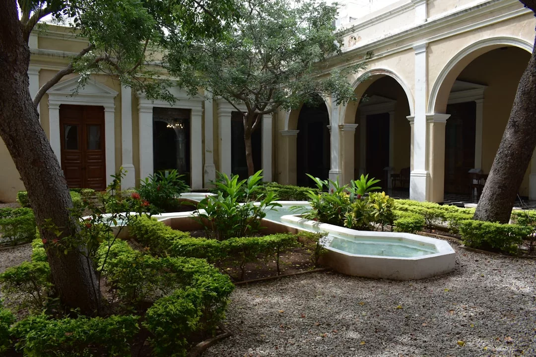 Patio con fuente central, plantas verdes, setos recortados, árboles, suelo de grava y pasarelas arqueadas en un edificio histórico de Mallorca que rezuma lujo.