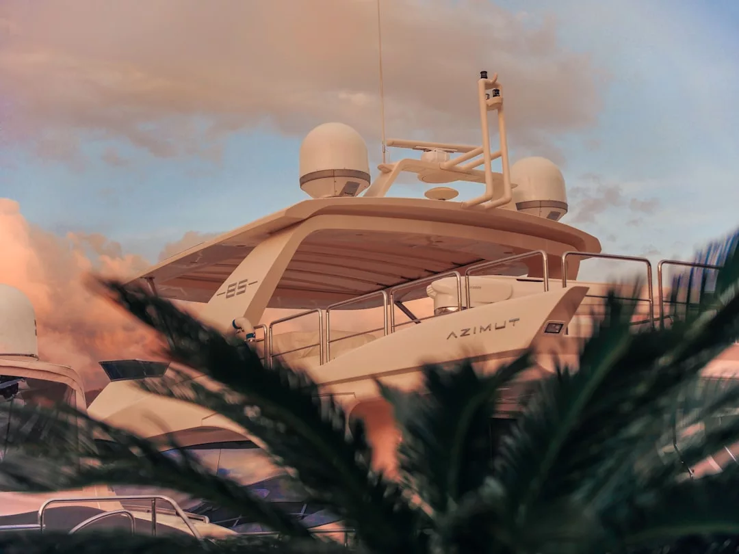 Un yate de lujo con la etiqueta "Azimut" atracado en Mallorca, con cúpulas de radar en el techo y hojas de palmera ocultando parcialmente la vista, bajo un cielo nublado al atardecer: la encarnación del puro lujo.