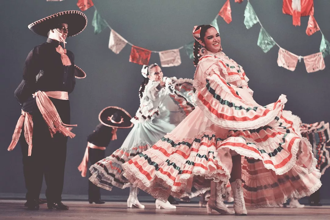 Bailarines ataviados con trajes tradicionales mexicanos interpretan folclore en el escenario, rodeados de coloridos vestidos y pancartas decorativas, aportando un toque de lujo a la celebración, que recuerda a las noches festivas de Mallorca.