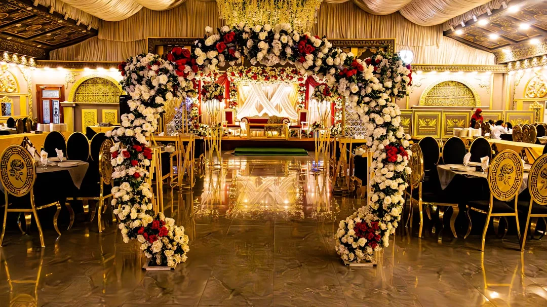 Un salón de banquetes lujosamente decorado en Mallorca con un arco floral circular, asientos elegantes, paredes ornamentadas y un escenario con telas drapeadas desprende puro lujo y sofisticación.