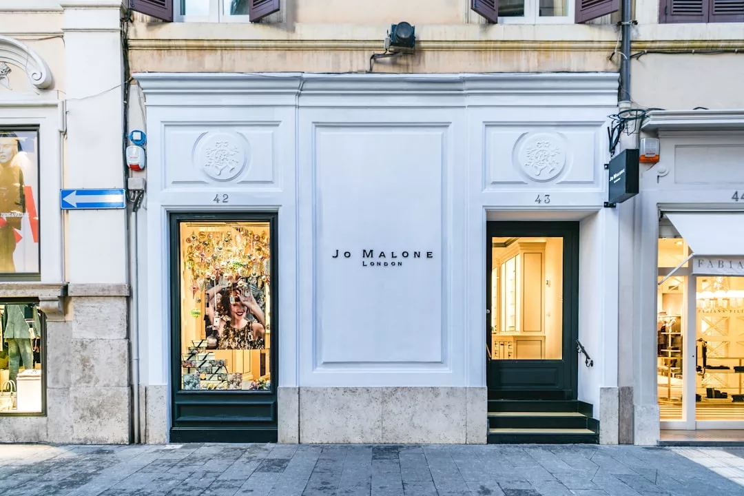 El exterior de una tienda Jo Malone London con fachada blanca, dos puertas de entrada y escaparates destila lujo en una calle empedrada de la pintoresca Mallorca.