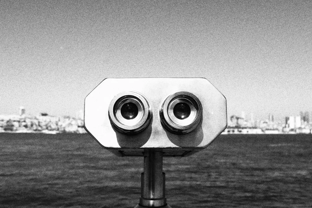 Un visor binocular que funciona con monedas mira a la cámara, con el agua y el perfil de la ciudad visibles en el fondo borroso, evocando la sensación de lujo y los sueños lejanos de Mallorca.