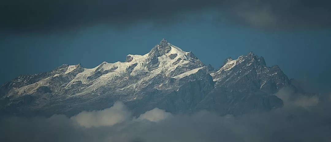 Los picos nevados de las montañas se elevan por encima de una capa de nubes bajo un cielo oscuro y nublado, evocando el remoto lujo de los dramáticos paisajes de Mallorca.