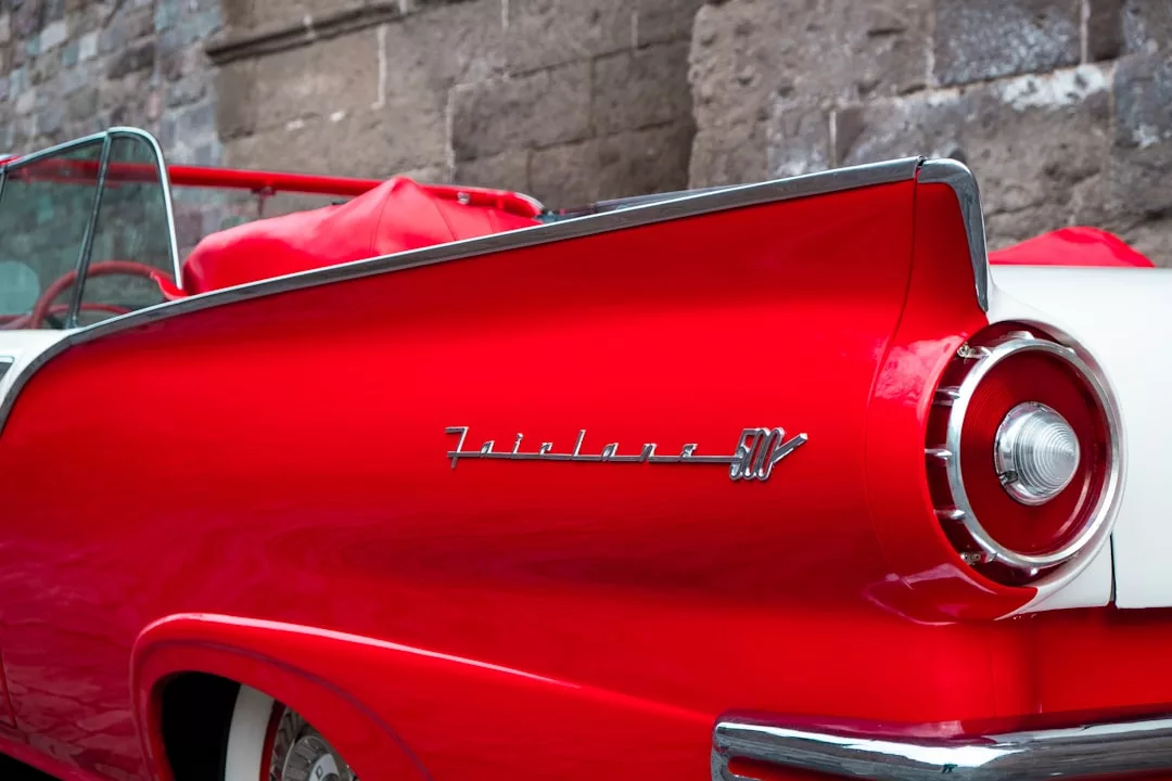 Primer plano de la parte trasera y la aleta trasera de un Ford Fairlane 500 Skyliner descapotable rojo, que irradia lujo mientras está aparcado frente a un muro de piedra, perfecto para los amantes de los coches clásicos que exploran Mallorca.