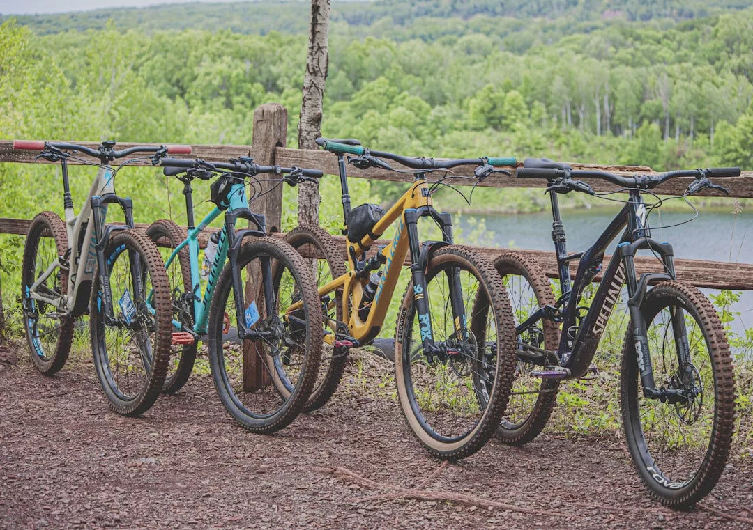 Cuatro bicicletas de montaña están aparcadas junto a una valla de madera con vistas a un río y a un exuberante paisaje boscoso de Mallorca: un entorno idílico para quienes buscan el lujo y la aventura al aire libre.