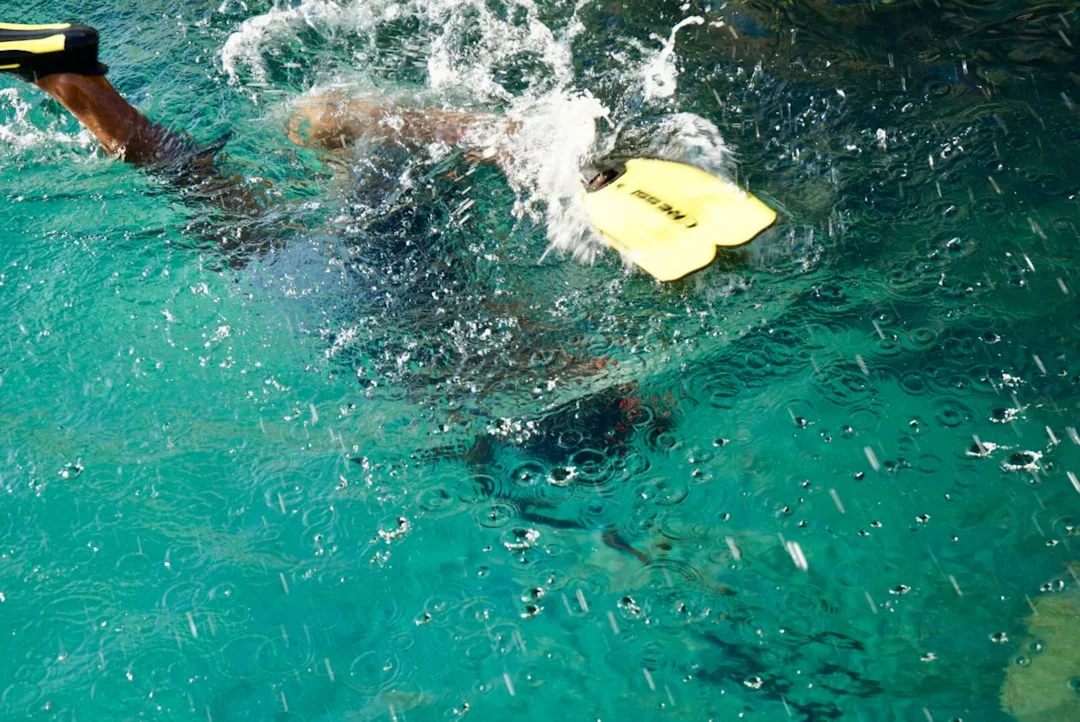 Una persona disfruta de un toque de lujo mientras nada bajo el agua en una piscina, llevando aletas de natación amarillas y haciendo chapoteos en la superficie, evocando el vibrante espíritu de Mallorca.