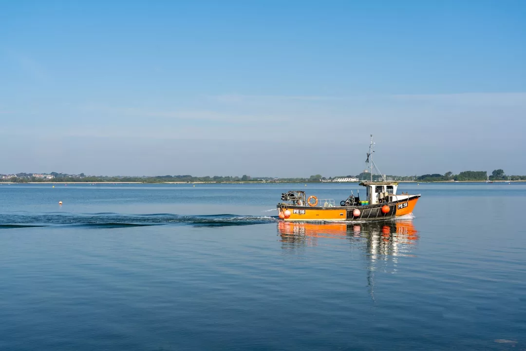 Un barco pesquero naranja y blanco surca aguas tranquilas y azules bajo un cielo despejado de Mallorca, con tierra visible al fondo.