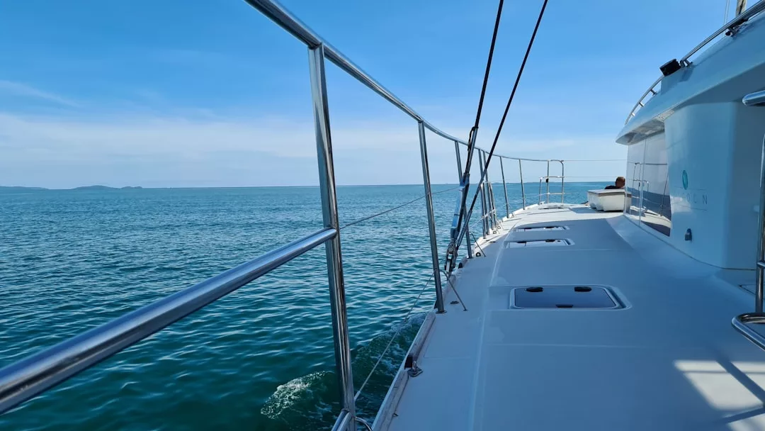 Vista desde la cubierta de un barco de lujo que navega por aguas tranquilas y azules bajo un cielo despejado, con barandillas metálicas y tierra lejana -Mallorca- visible en el horizonte.