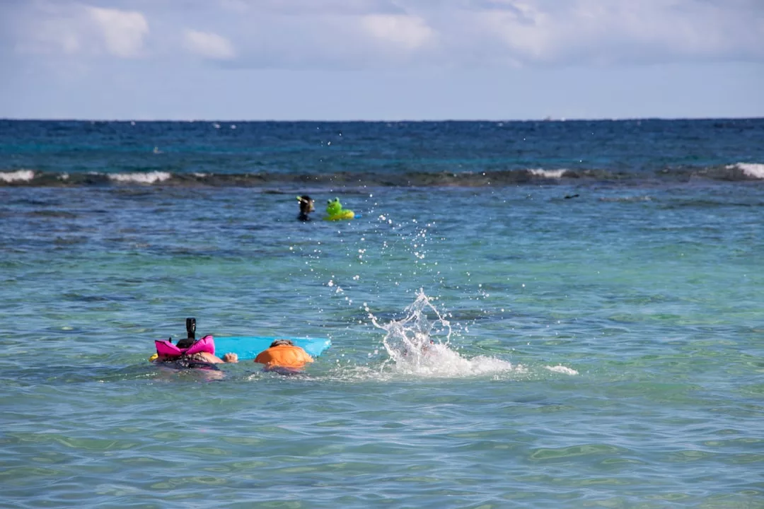 Dos personas con tubo y flotador nadan cerca de la superficie centelleante de Mallorca; las salpicaduras brillan a la luz del sol, mientras otra persona disfruta del lujo de flotar más lejos en el océano.