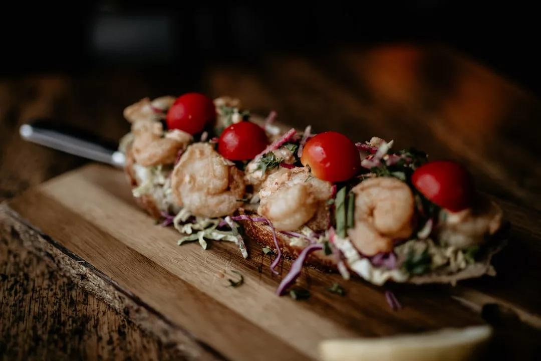 Un bocadillo abierto con gambas, verduras ralladas y tomates cherry enteros sobre una tabla de madera, que aporta un toque de Lujo que recuerda a los sabores costeros de Mallorca.