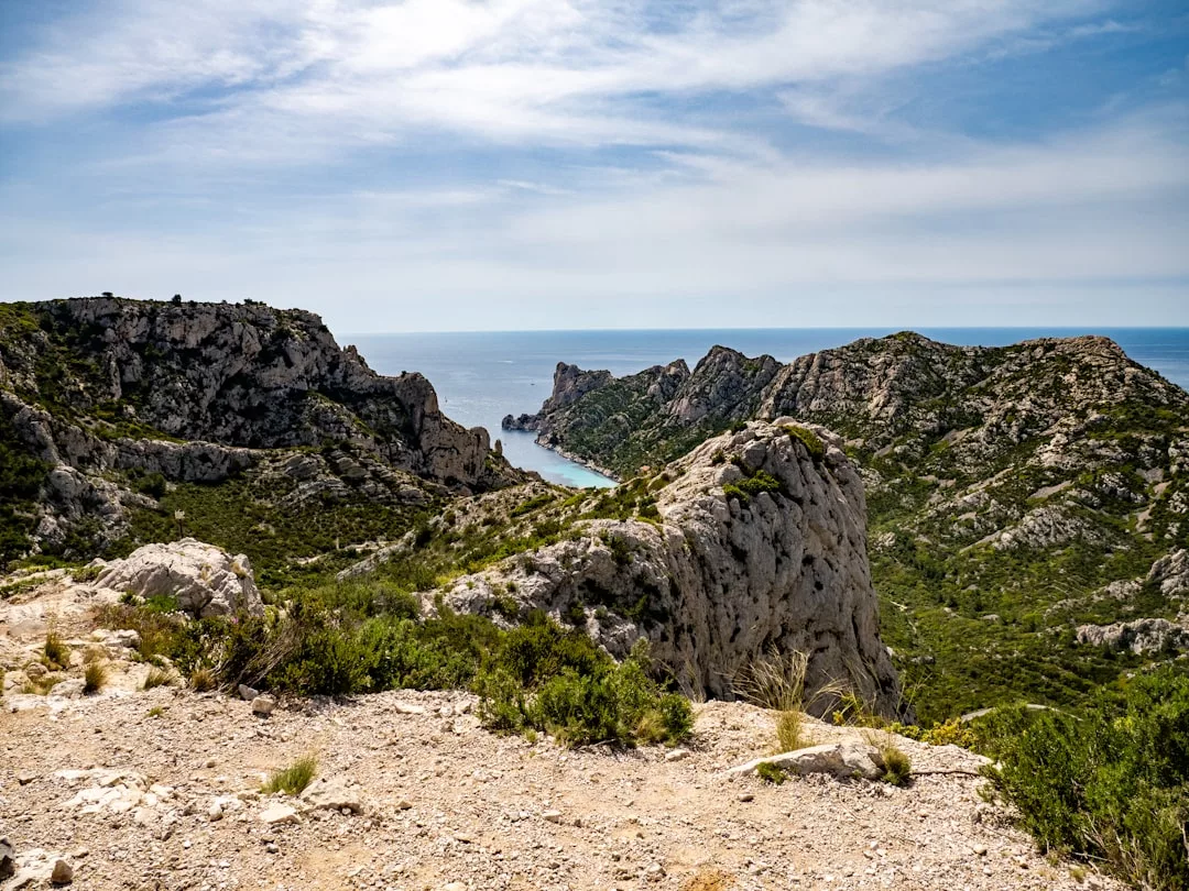 Acantilados rocosos y arbustos verdes descienden hasta una pequeña bahía de aguas azules en Mallorca, enmarcada por escarpadas colinas y un cielo parcialmente nublado: puro lujo en la llamativa costa de la isla.