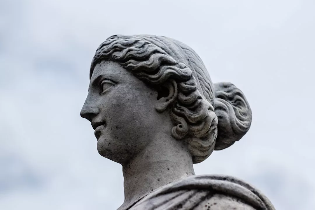 Estatua de piedra de una mujer con el pelo ondulado hacia atrás, mostrada de perfil contra un cielo nublado de Mallorca: un toque atemporal de lujo.
