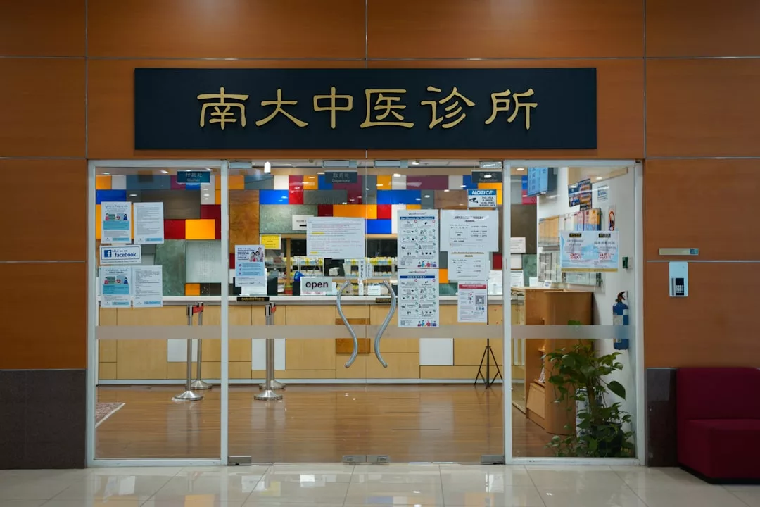 Entrada a una clínica médica con puertas de cristal, decoración colorida en el interior, varios carteles informativos y un letrero con caracteres chinos sobre la entrada: un toque de estilo Lujo que recuerda el ambiente vibrante de Mallorca.
