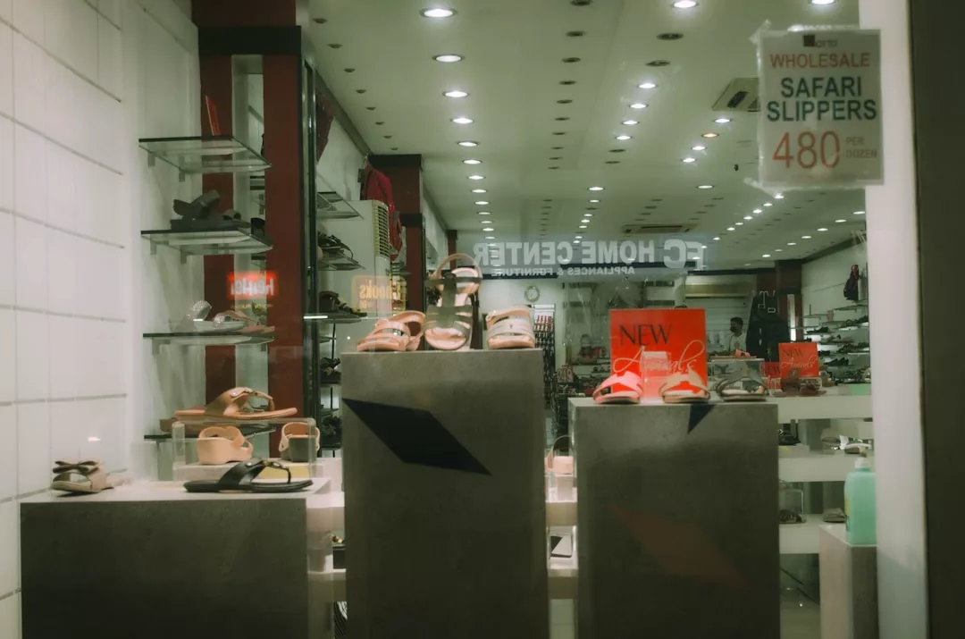 Escaparate de la tienda con varias sandalias sobre pedestales, con carteles que anuncian "Safari Slippers" por 480 y una promoción "New Arrival". Los diseños inspirados en Mallorca y los toques de lujo realzan el encanto de la colección.