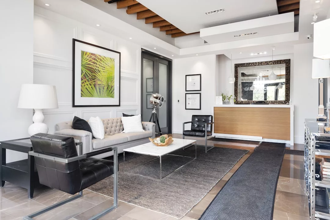 Moderno vestíbulo de oficina con un sofá beige, sillones negros, mesa de centro, arte en la pared y un mostrador de recepción con un gran marco de espejo: un espacio acogedor que refleja el lujo contemporáneo de Mallorca.