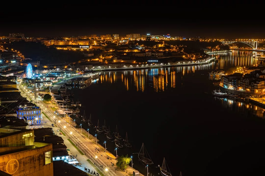 Un paisaje urbano nocturno con edificios iluminados, un río que refleja las luces de la ciudad, barcos atracados en la orilla y un puente al fondo evoca el lujo de la vibrante costa de Mallorca.