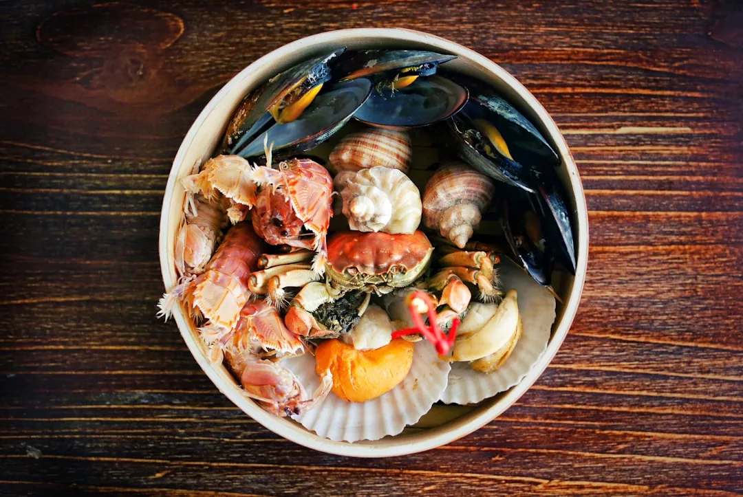 Un cuenco de marisco cocido variado, como mejillones, gambas, almejas, caracoles y vieiras, evoca los sabores de Mallorca y añade un toque de lujo a cualquier mesa de madera.