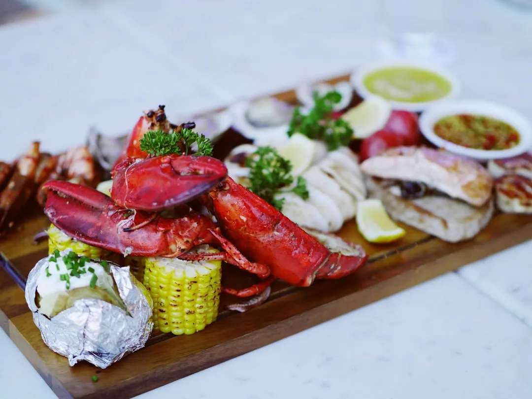 Una fuente de madera con marisco variado, como pinzas de langosta, gambas, pescado, mazorcas de maíz, patatas asadas, gajos de limón y salsas para mojar: perfecto para saborear Mallorca y un toque de lujo en su mesa.