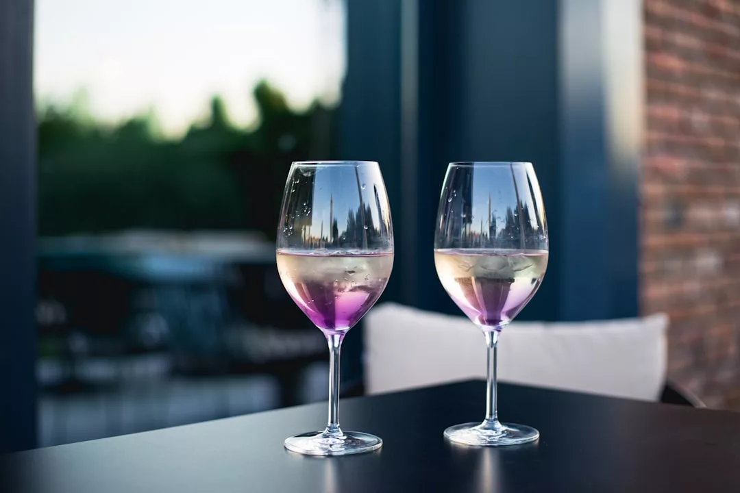 Dos copas de vino con una bebida rosácea y cubitos de hielo reposan sobre una mesa oscura al aire libre, captando el lujo de Mallorca mientras los reflejos del entorno de la isla brillan en el cristal.