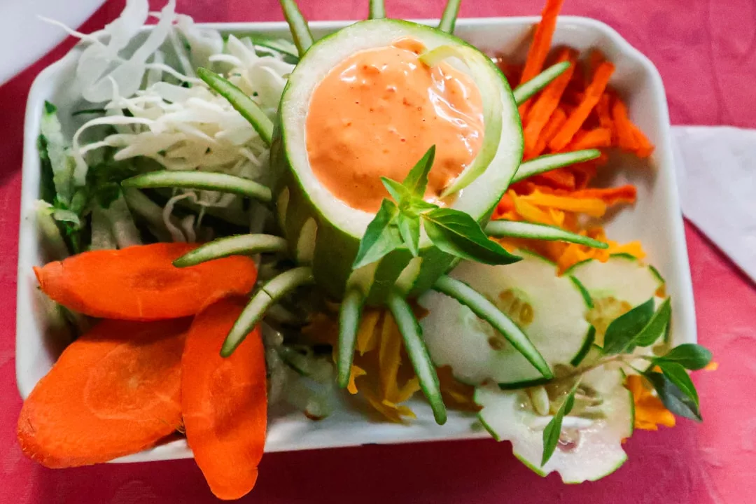 Un plato de verduras en rodajas variadas, incluyendo zanahoria, pepino y repollo, bellamente dispuestas en el verdadero estilo Lujo con una taza central de pepino llena de aderezo de naranja - un refrescante sabor de Mallorca.