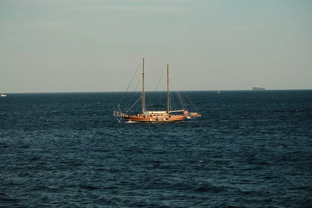 Un velero de dos mástiles flota sobre las tranquilas aguas de un océano azul intenso bajo un cielo despejado de Mallorca, irradiando un aire de lujo y tranquilidad.