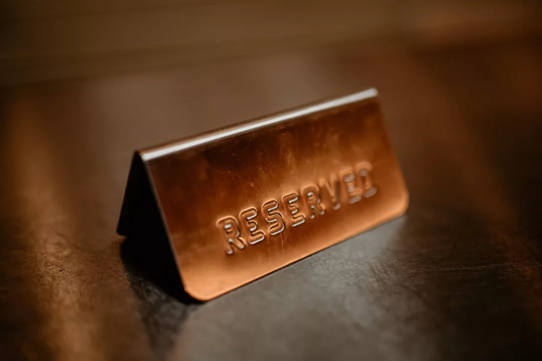 Un letrero metálico de "Reservado" se asienta sobre una superficie marrón, aludiendo al lujo y la exclusividad que se encuentran en los mejores locales de Mallorca, marcando la zona o la mesa como especialmente reservada para alguien.