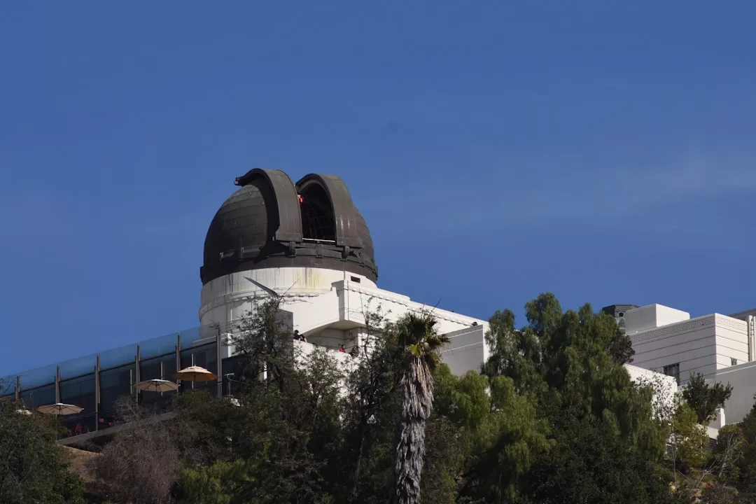 Un edificio observatorio blanco con una gran cúpula y tejado abierto, rodeado de árboles bajo un cielo azul despejado, ofrece un toque de lujo en medio de la belleza natural de Mallorca.