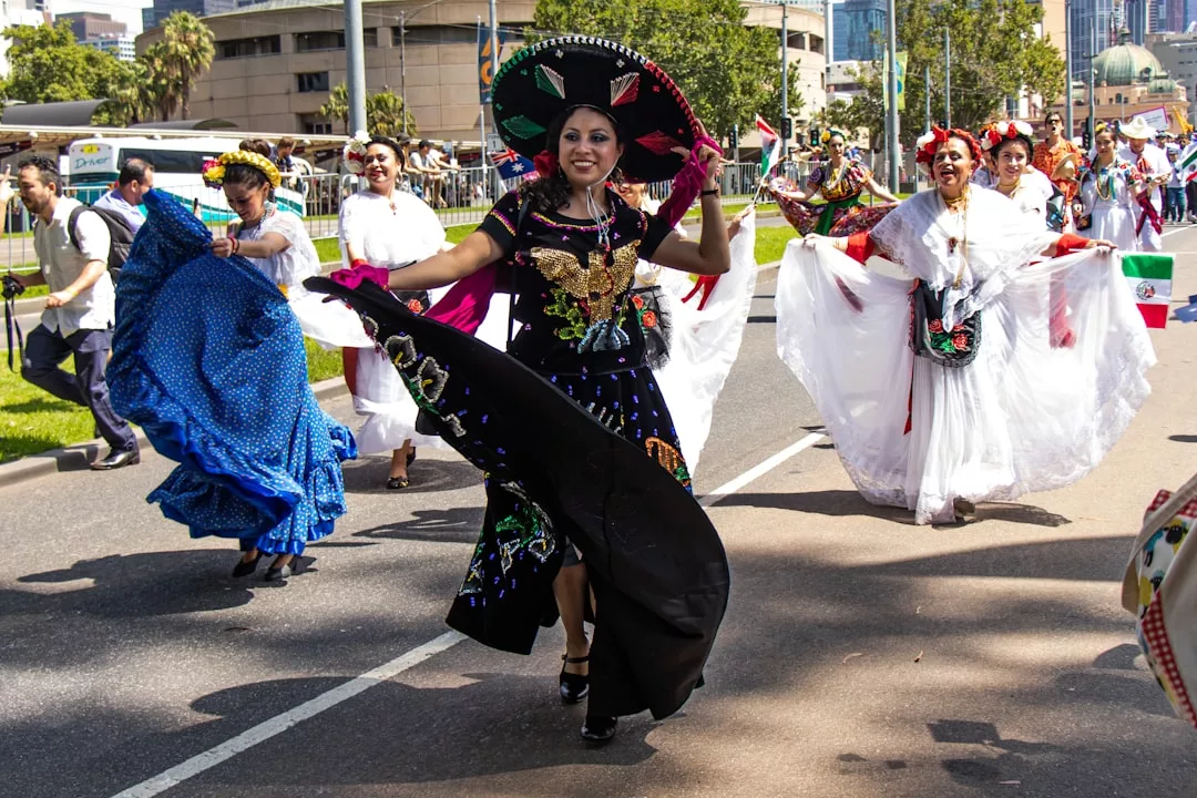 Mujeres vestidas con trajes tradicionales mexicanos bailan en un desfile callejero a la luz del día, aportando un toque de lujo y vitalidad que recuerda a Mallorca, con los espectadores y los edificios de la ciudad enmarcando la animada escena.