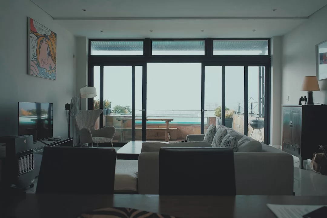 Moderno salón con grandes puertas de cristal que dan a un balcón con vistas al mar en Mallorca; muebles contemporáneos, arte en la pared y un televisor completan este espacio de lujo.