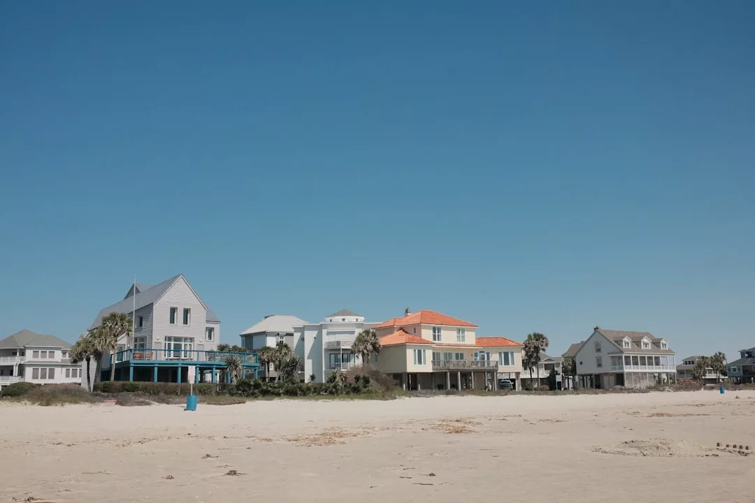 Fila de casas en primera línea de playa en Mallorca, mostrando varios estilos arquitectónicos de lujo, bajo un cielo azul claro y vistas desde la playa de arena en primer plano.