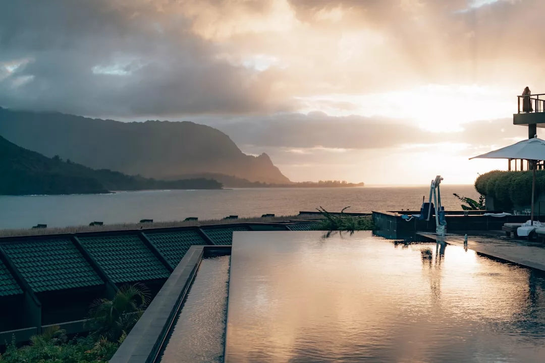 Piscina infinita con vistas al océano al atardecer en Mallorca, con montañas y nubes al fondo y tumbonas Lujo junto a la piscina.