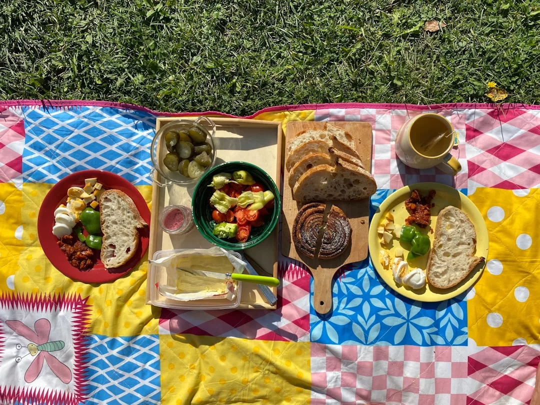 Un picnic sobre una colorida manta con platos de pan, huevos, queso, ensalada, encurtidos y un pastelito sobre una hierba exuberante ofrece un toque de lujo mallorquín en cada detalle.