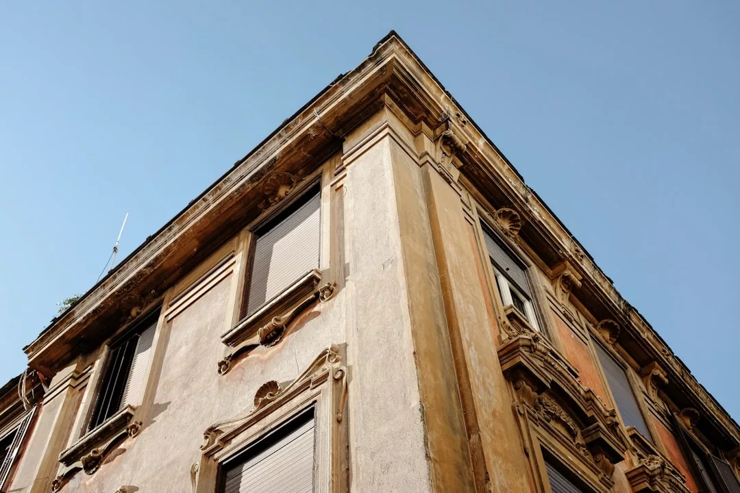 Vista desde un ángulo bajo de un edificio antiguo de color beige con contraventanas cerradas y detalles arquitectónicos decorativos en Mallorca, que capta una sensación de lujo contra un cielo azul claro.