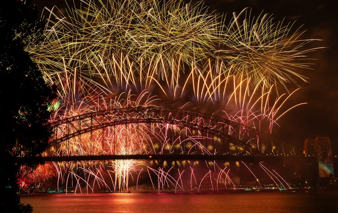 Coloridos fuegos artificiales estallan por encima de un gran puente sobre el agua por la noche en Mallorca, iluminando el cielo con una sensación de lujo y reflejándose brillantemente en la superficie de abajo.