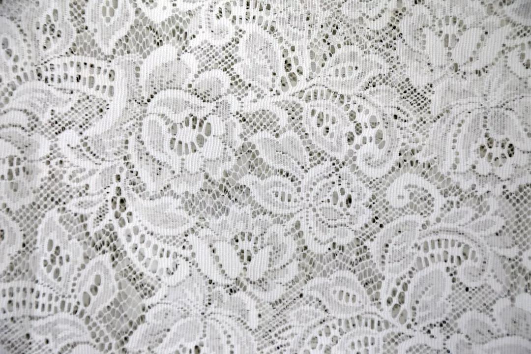 Primer plano de tejido de encaje blanco con motivos florales y fondo de malla fina, que evoca la elegancia de Lujo en Mallorca.