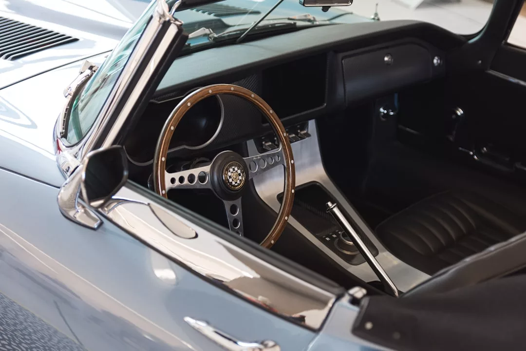 Vista interior de un coche descapotable clásico que destila lujo, con volante de madera, cambio de marchas manual y asientos de cuero negro, perfecto para recorrer las pintorescas carreteras de Mallorca.