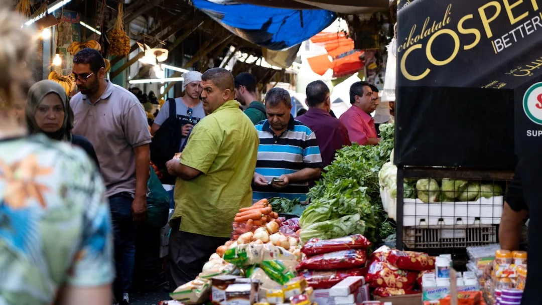 La gente compra en un mercado al aire libre de Mallorca, ojeando productos frescos y envasados, con varios puestos y un toque de lujo visible en el bullicioso pasillo.